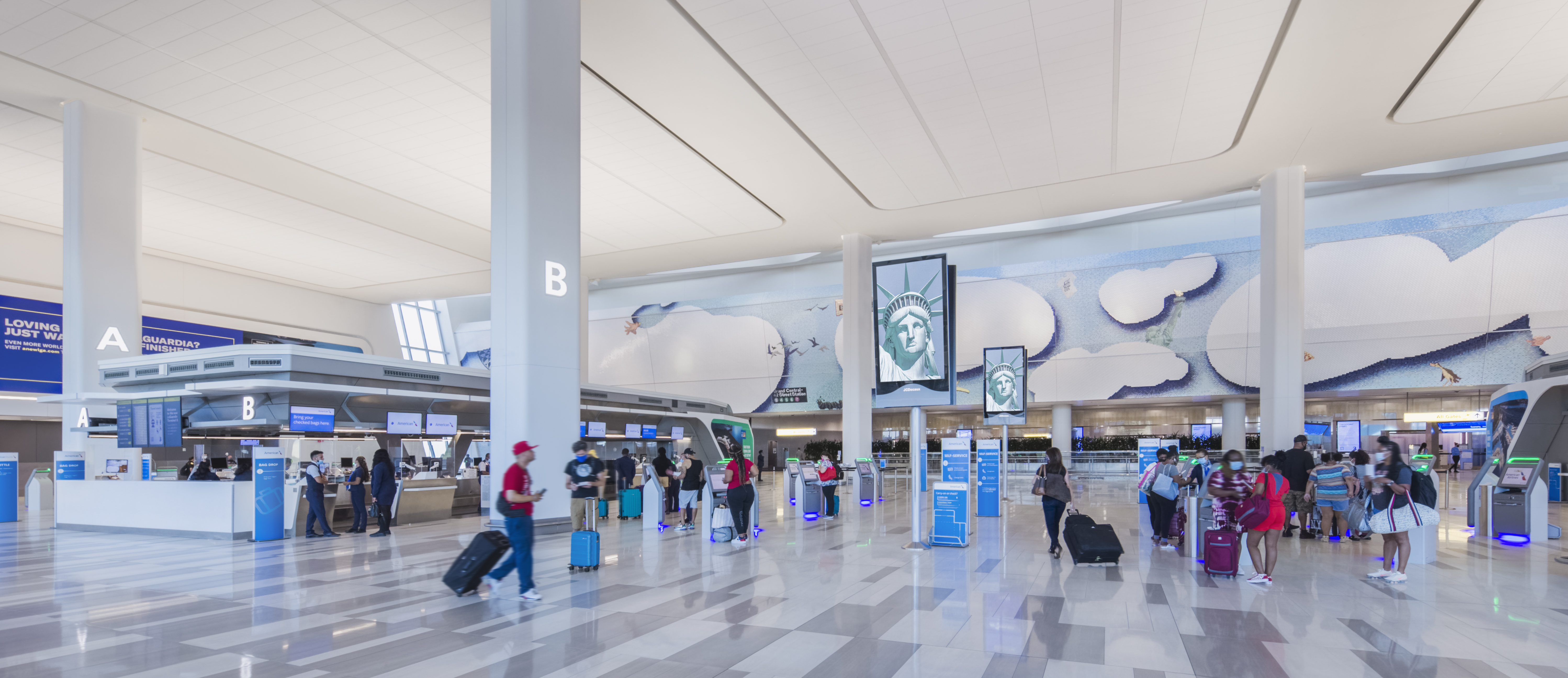 Vue d&rsquo;ensemble de la zone d&rsquo;enregistrement de l&rsquo;a&eacute;rogare B de l&rsquo;a&eacute;roport LaGuardia, qui pr&eacute;sente un am&eacute;nagement ouvert et &eacute;clair&eacute;, des couloirs d&eacute;gag&eacute;s, des bornes libre-service ainsi que des passag&egrave;res et des passagers qui y circulent librement.