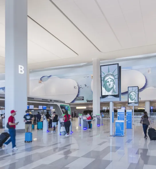 Vue d&rsquo;ensemble de la zone d&rsquo;enregistrement de l&rsquo;a&eacute;rogare B de l&rsquo;a&eacute;roport LaGuardia, qui pr&eacute;sente un am&eacute;nagement ouvert et &eacute;clair&eacute;, des couloirs d&eacute;gag&eacute;s, des bornes libre-service ainsi que des passag&egrave;res et des passagers qui y circulent librement.