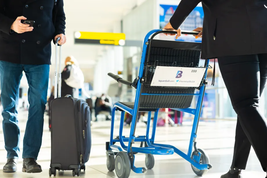 1.	Gros plan sur une personne[AN1.1] qui pousse une valise &agrave; roulettes &agrave; c&ocirc;t&eacute; d&rsquo;une femme qui pousse un fauteuil roulant de l&rsquo;a&eacute;roport &agrave; l&rsquo;a&eacute;rogare B de LaGuardia.